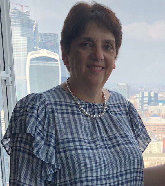 A woman smiling at the camera. She is wearing a patterned blouse.