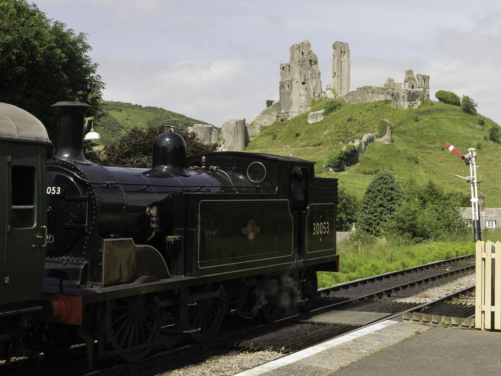 A picturesque image of a a castle ruin on a hill. In the foreground is a steam train.