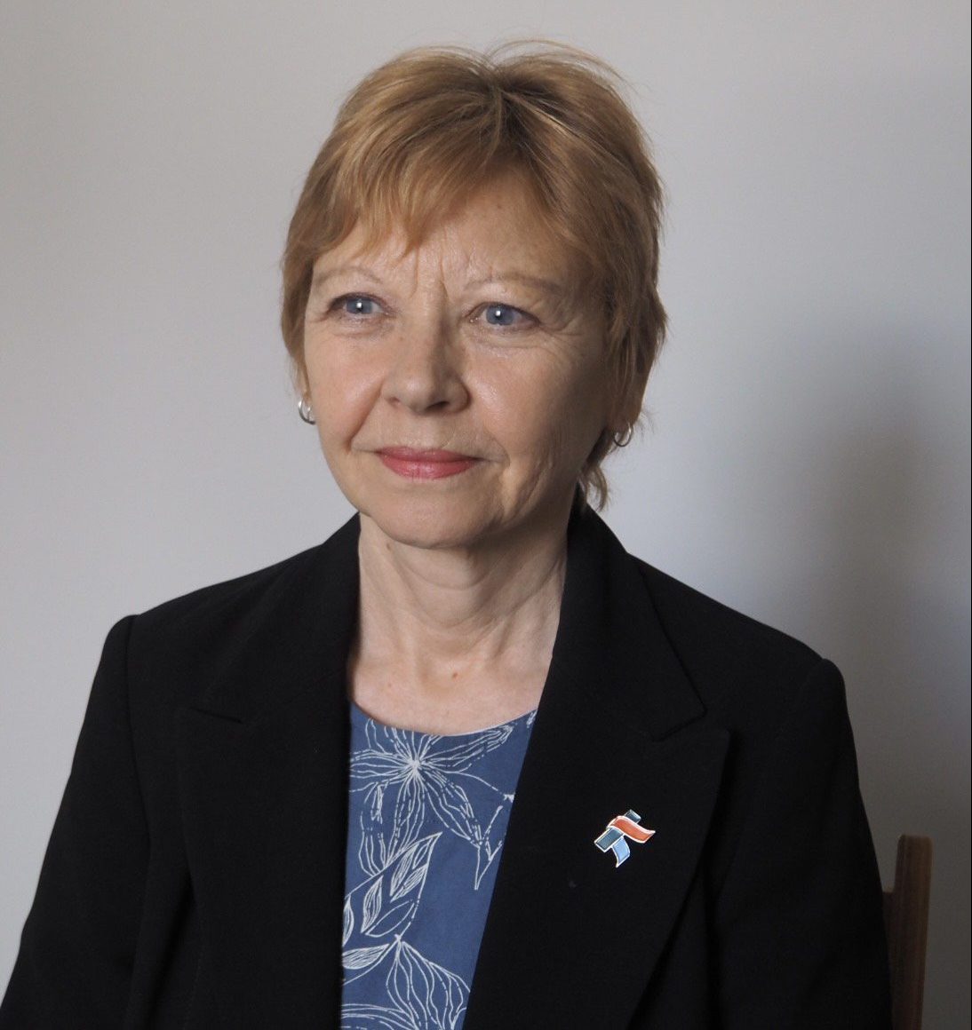 A woman smiling at the camera. She is wearing a blue blouse and a black jacket.