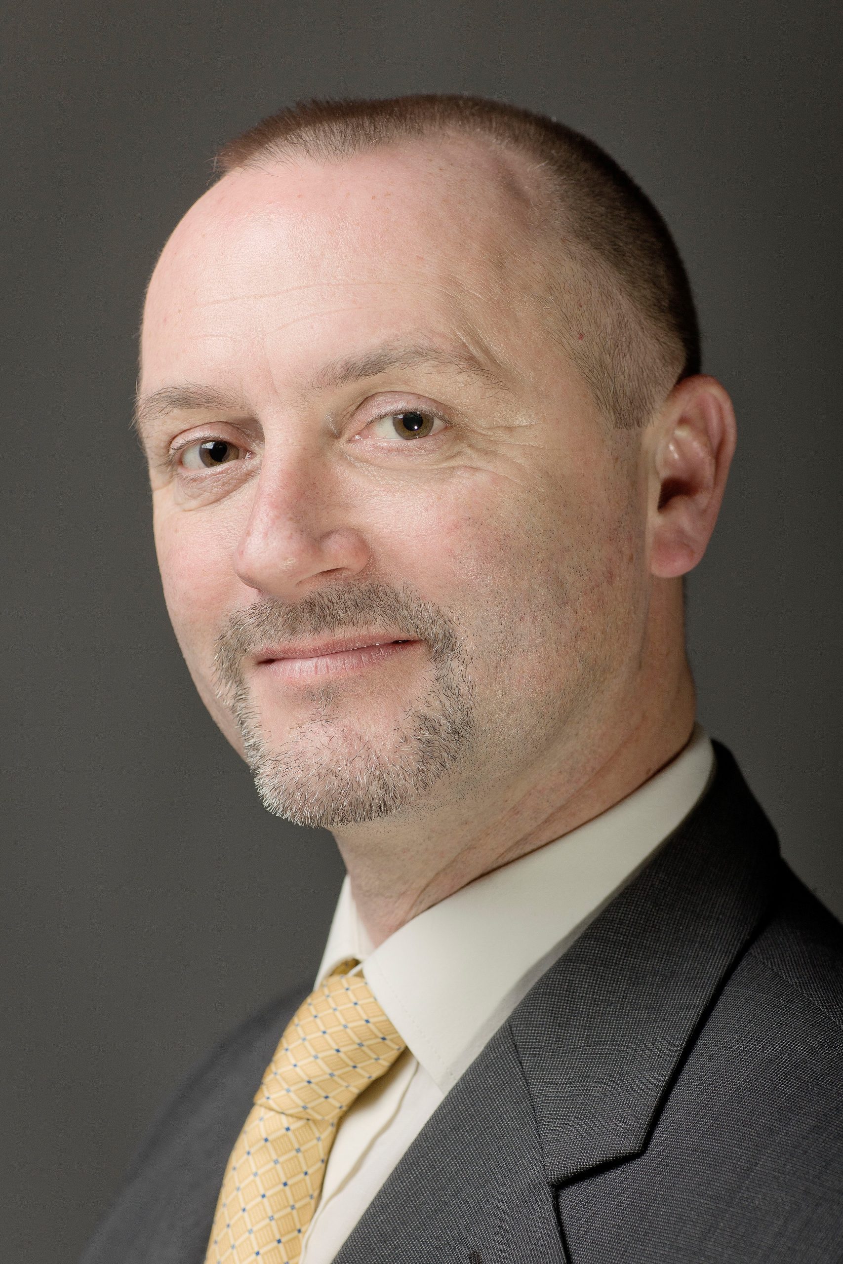 A man smiling at the camera. He is wearing a shirt and tie.
