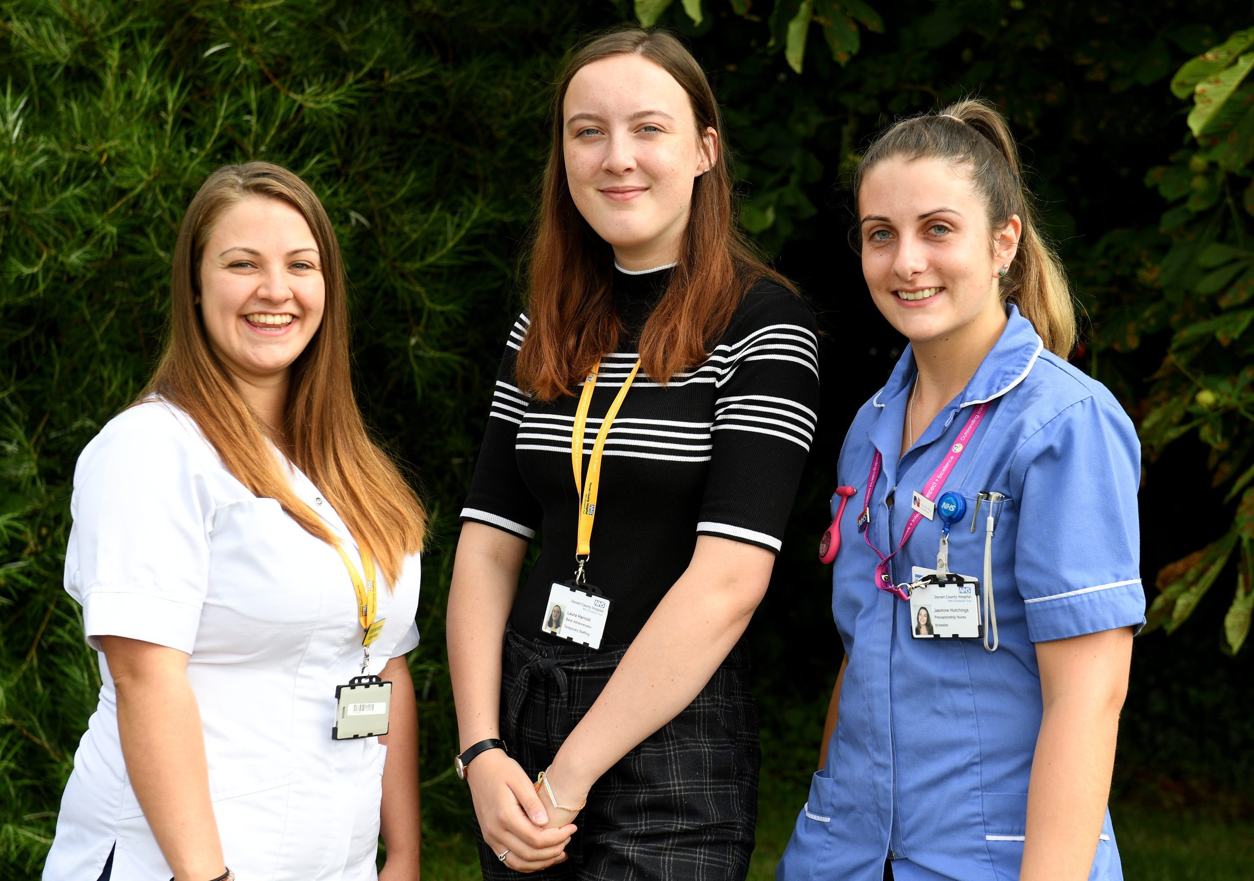 Three healthcare workers standing together, smiling at the camera.