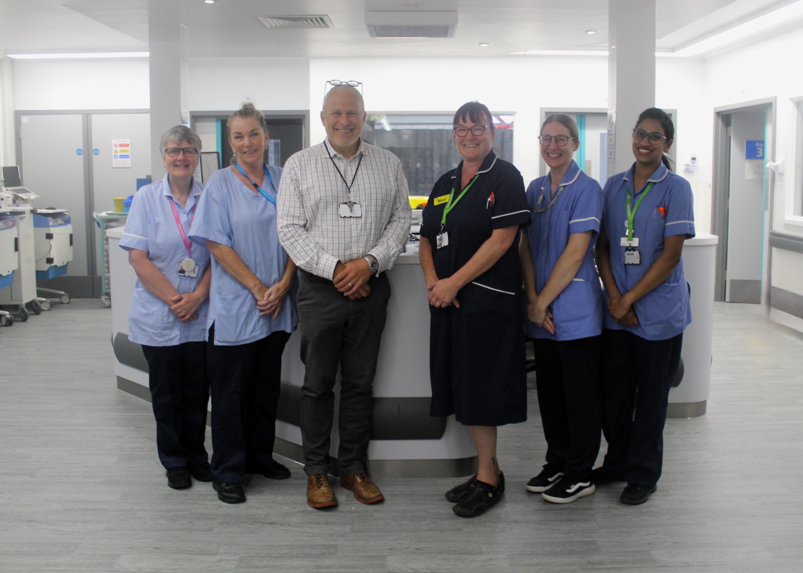 A group of healthcare staff standing in a ward. They are looking at the camera and smiling