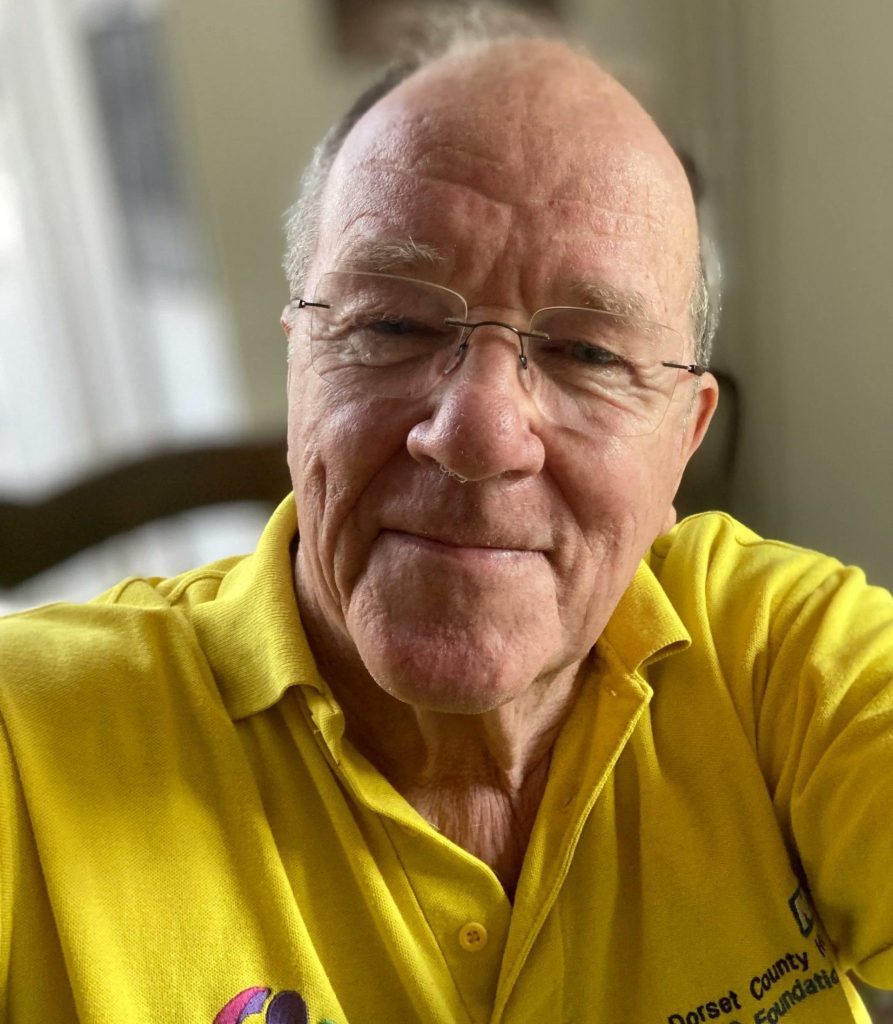 A man in a yellow t-shirt, smiling at the camera.