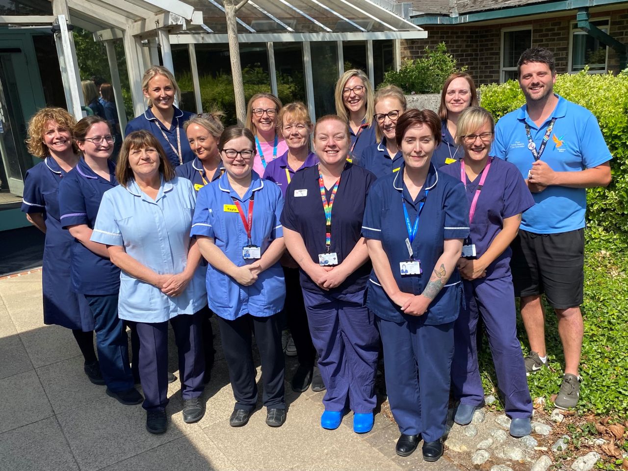 A group of healthcare staff standing outside a building in the sunshine. They are all smiling at the camera.