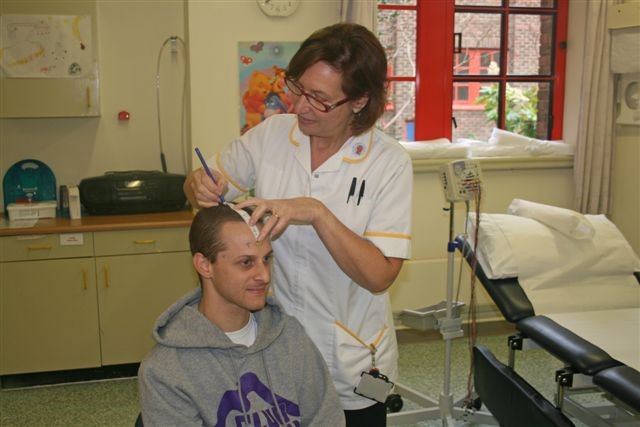 A healthcare worker is helping a patient prepare for a test on their head.