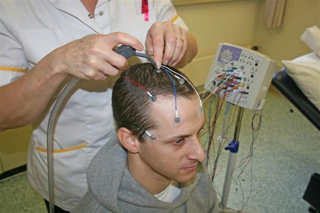 A healthcare worker is attaching wires to a patient's head to be able to perform a test. A machine is in the background.