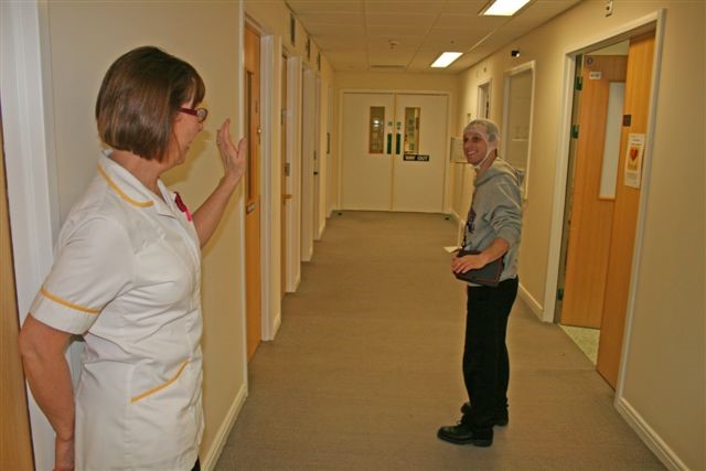 A healthcare worker waves goodbye to a patient in a hospital corridor.