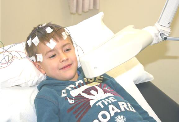A child lying on a hospital bed with wires on his head. A light is flashing in front of him.