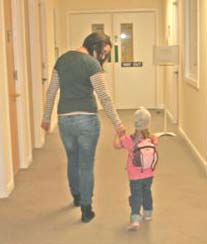 A young girl walking down a hospital corridor holding her mother's hand.