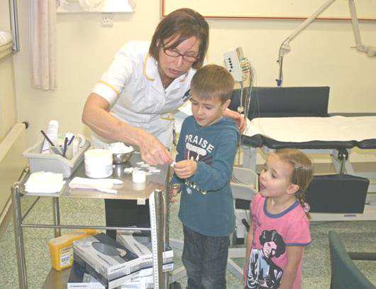 A healthcare worker showing two children the items she will be using for their hospital tests.
