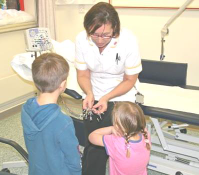 A healthcare worker showing two young children the items she will be using for their hospital tests.