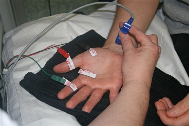 Stickers and wires on a person's hand. Another person is holding a medical device near their wrist.