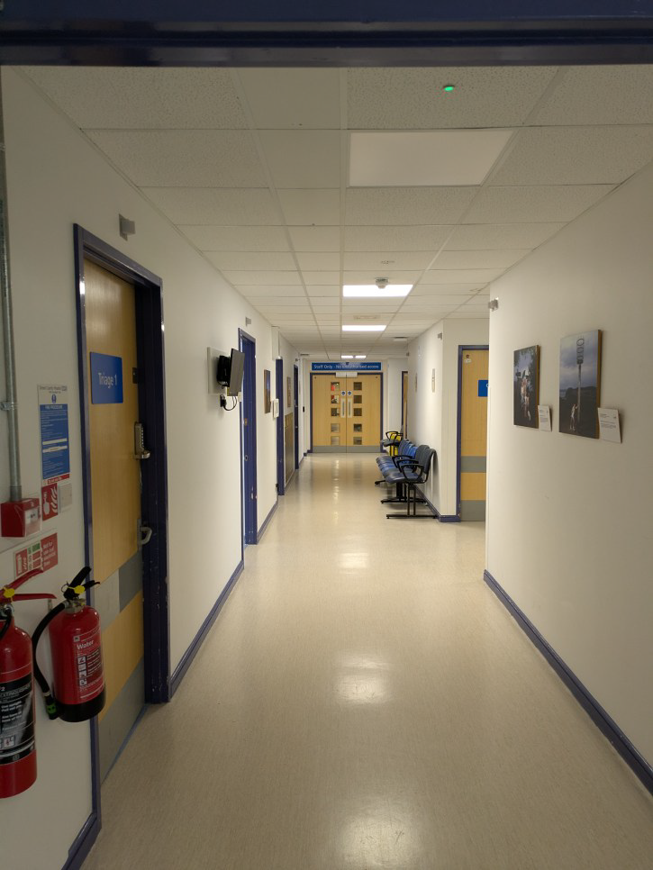 A corridor in a hospital. There are a line a chairs on the right.