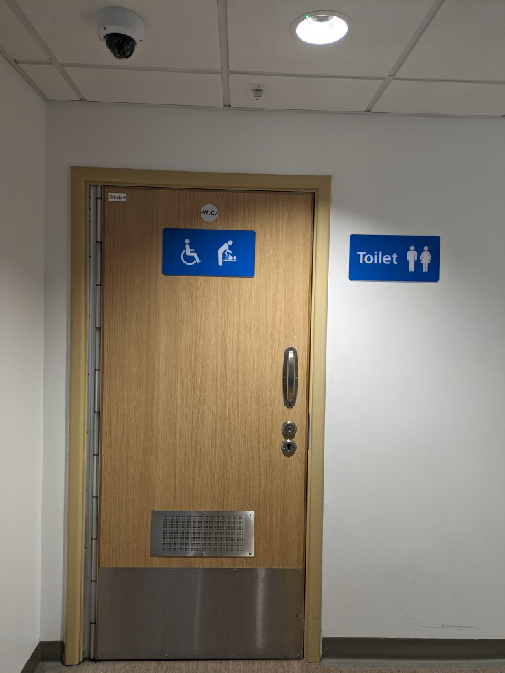 A wooden door in a corridor. There is a sign that reads 'Toilet' next to the door.