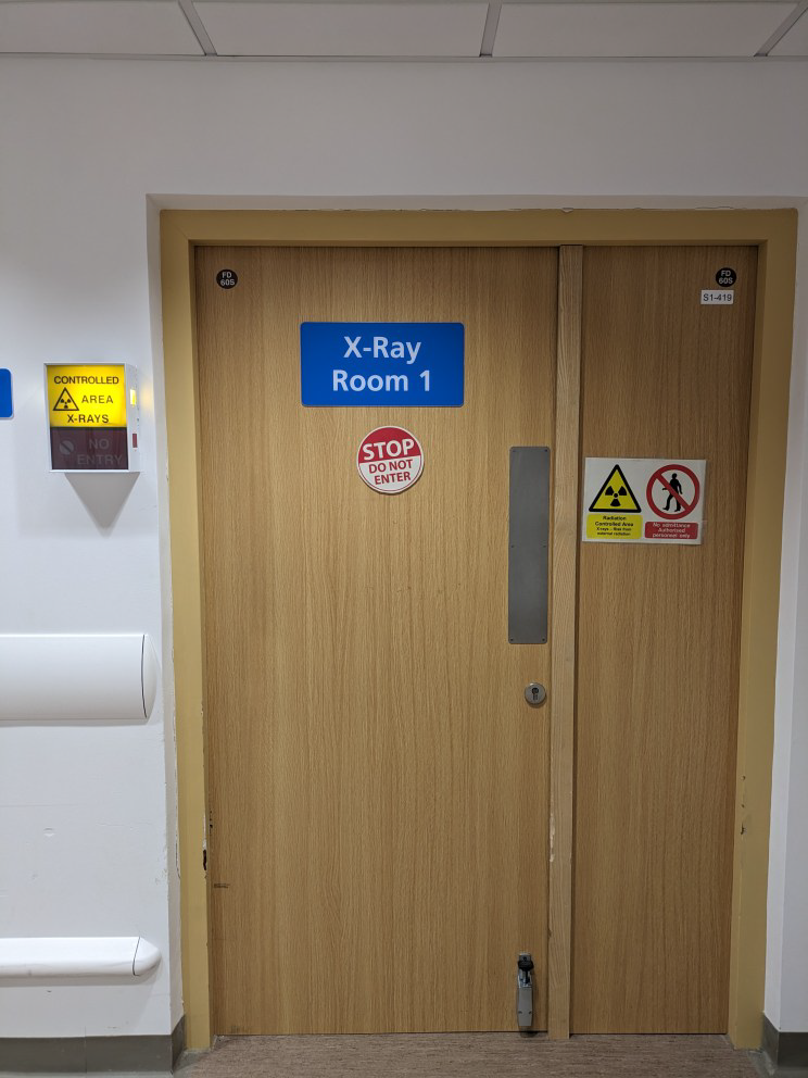 A door with a blue sign that reads 'X-Ray Room 1'. Underneath is a 'STOP DO NOT ENTER' sign.
