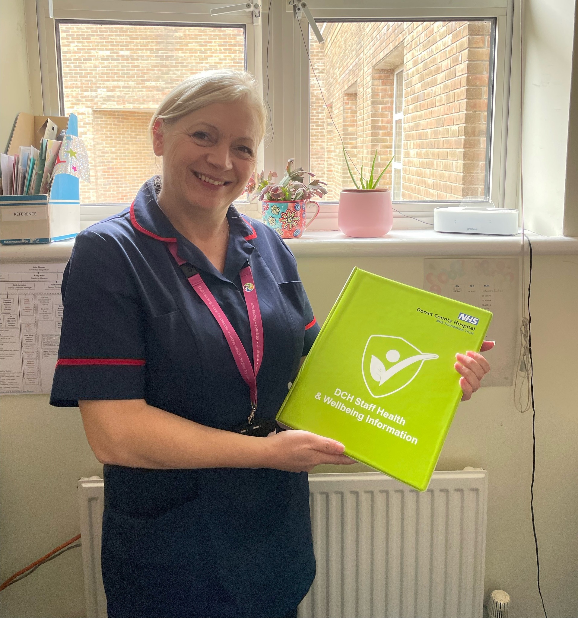 A hospital nurse holding a green folder titled 'DCH staff health and wellbeing information'.