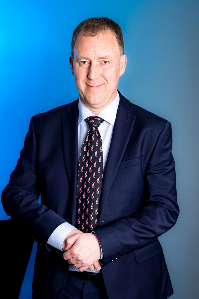 A person in a shirt and tie smiling at the camera.