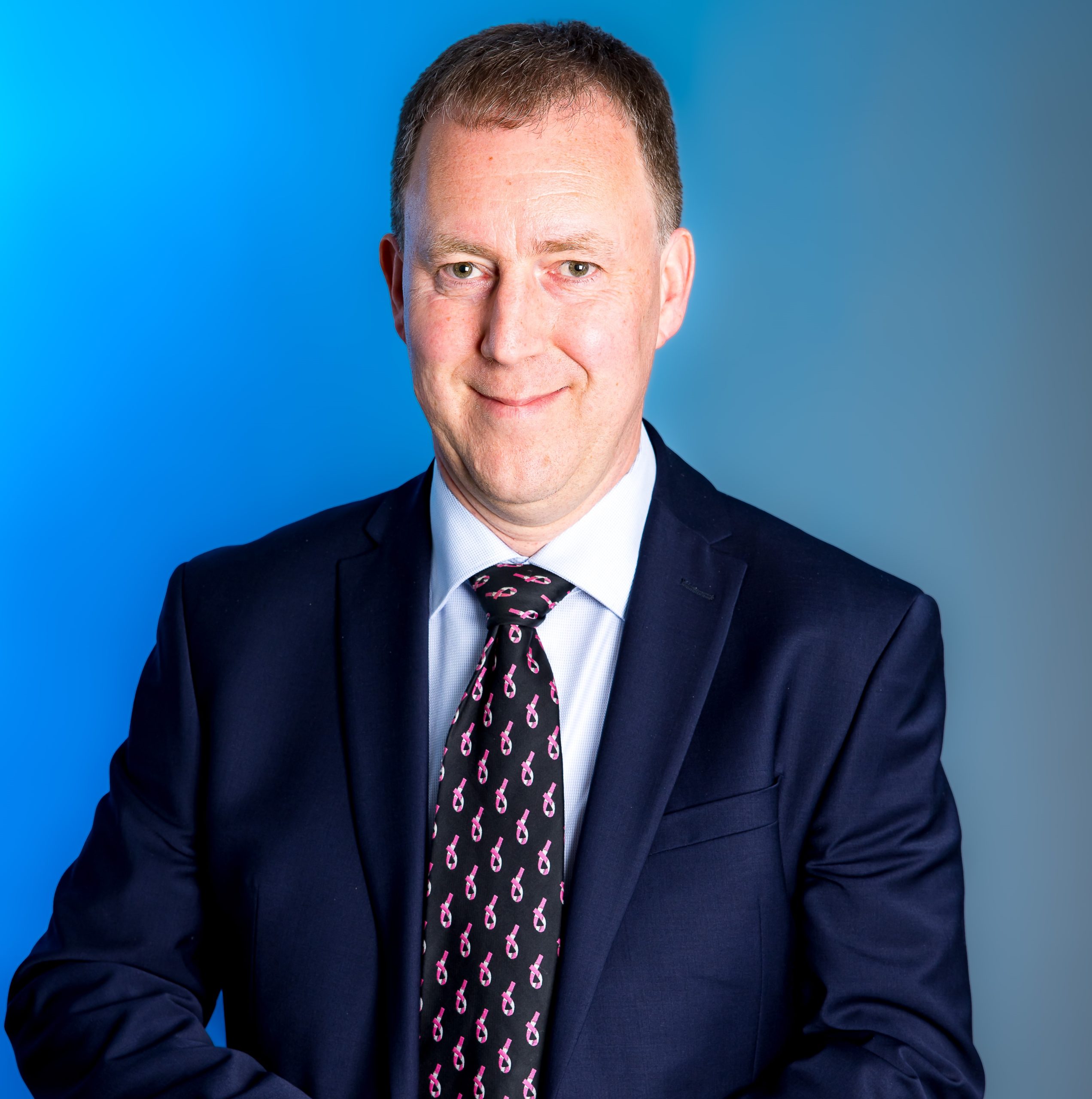A person in a shirt and tie smiling at the camera.