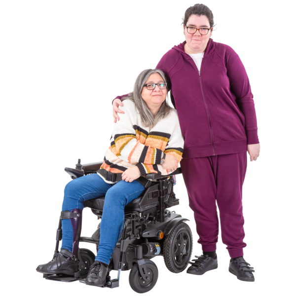 A person in a striped sweater sitting in a motorized wheelchair and another person in a purple tracksuit standing beside them, both looking at the camera.