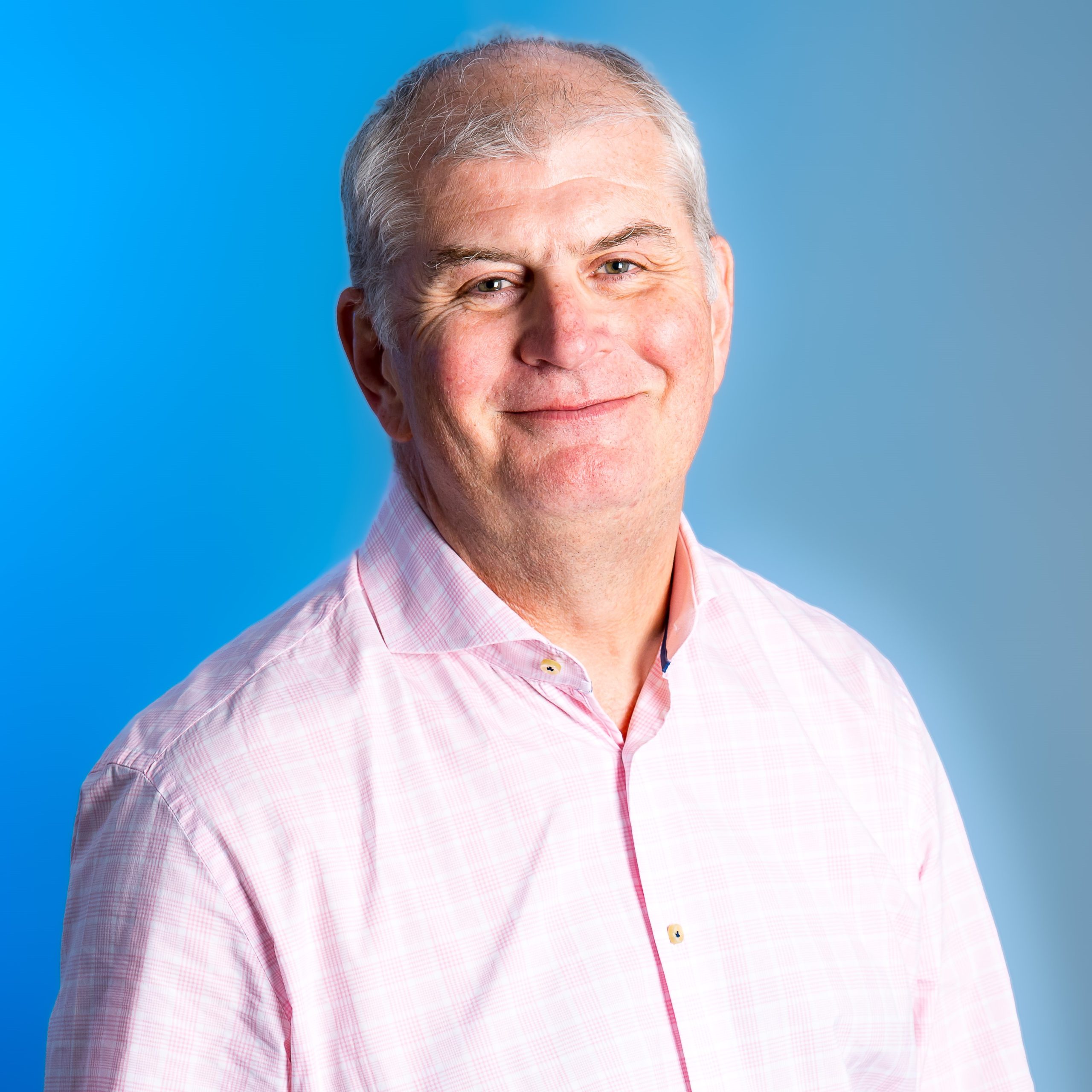 A man in a pink checked shirt, smiling at the camera.