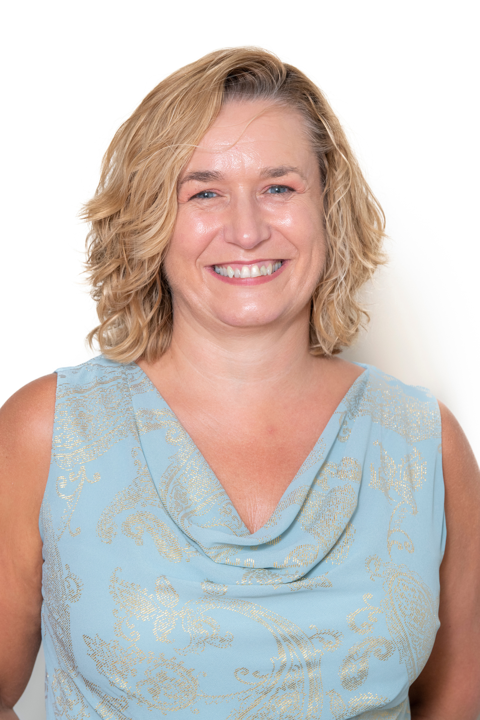 A woman smiling at the camera. She is wearing a blue blouse and is pictured in front of a white background.