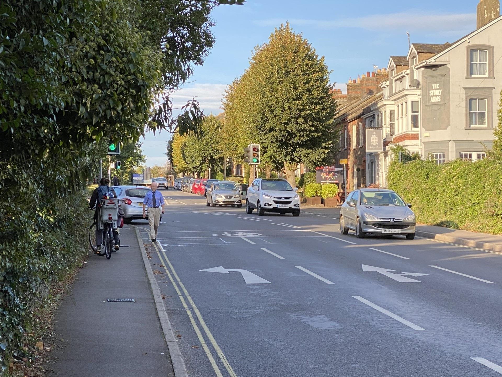 A junction of a road with a few cars. There is also a pedestrian and a person on a bike.