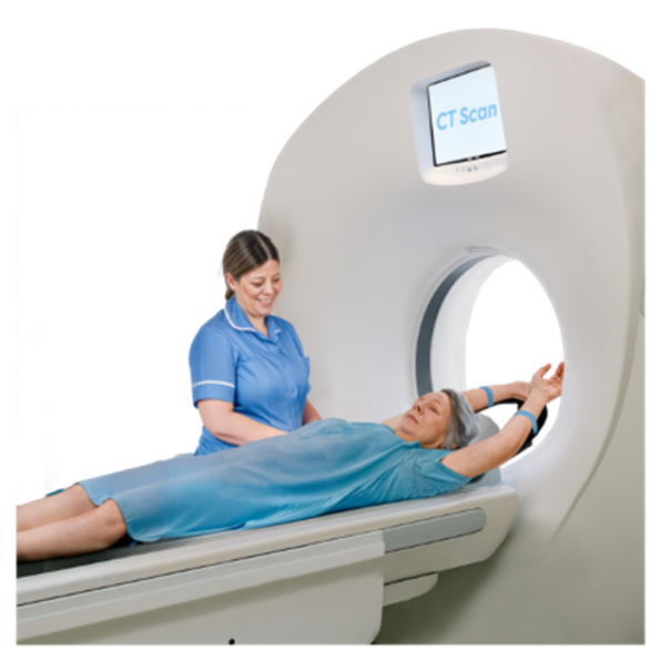 An individual in a hospital gown having a CT scan. A nurse is standing next to her smiling.