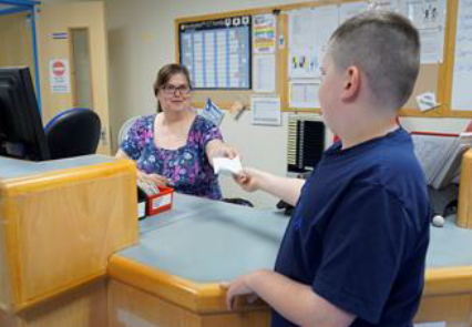 A person handing a letter to a professional behind a reception desk.